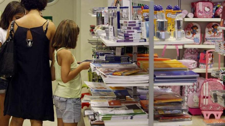 Una mujer con sus dos hijas, ante estanterías con material escolar. Foto Efe