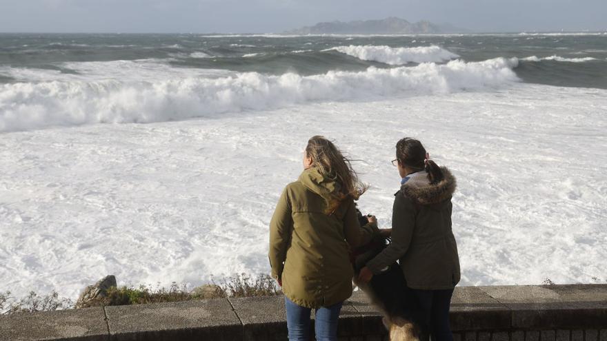 Dos jóvenes contemplan el oleaje desde el paseo de Baiona.