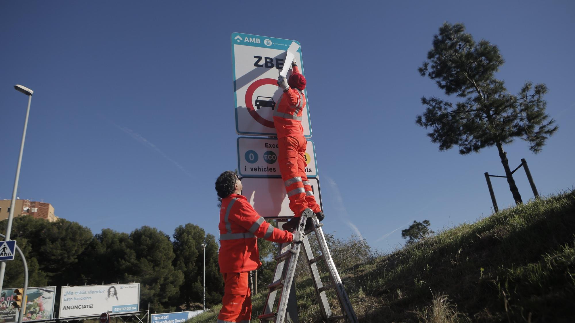 Dos operarios colocan la nueva señal de tráfico en una carretera de L'Hospitalet de Llobregat.