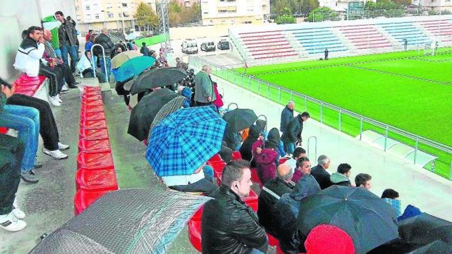 Los aficionados tienen que abrir los paraguas cuando llueve en la tribuna cubierta.