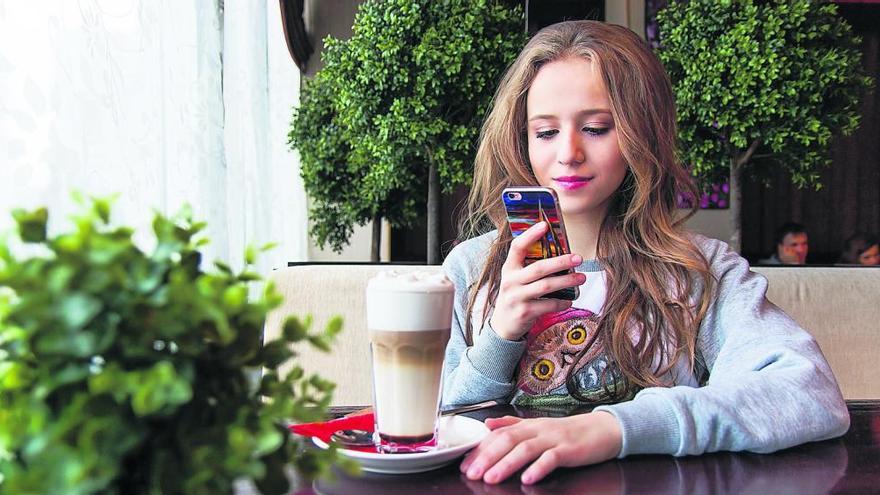 Una adolescente, mirando su móvil mientras se toma un batido.