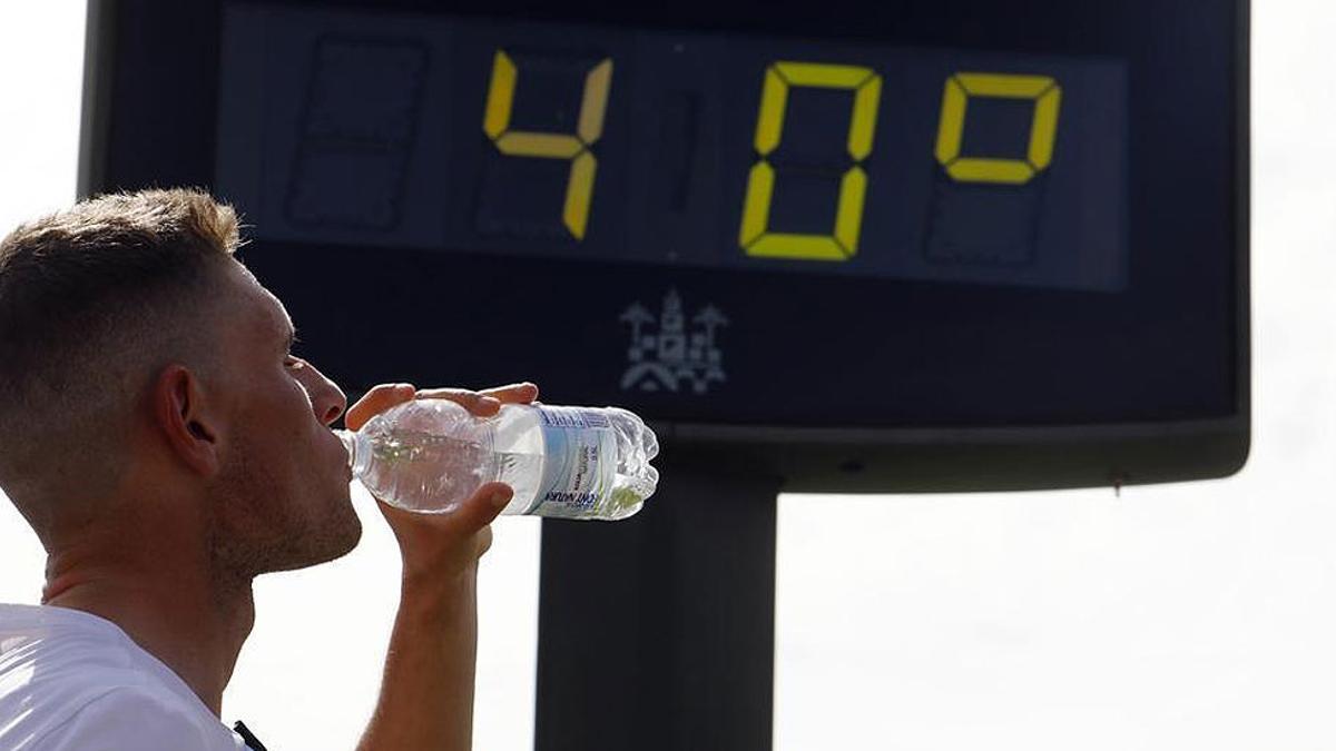 Un hombre bebe agua frente a un termómetro que marca 40 grados