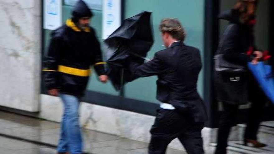 Un hombre trata de controlar su paraguas frente al viento.  //  Abella