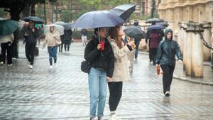 Varias personas se protegen de la lluvia bajo sus paraguas. A 9 de febrero de 2024, en Sevilla (Andalucía, España). La borrasca Karlotta activa avisos por lluvia, viento y oleaje en todas las provincias andaluzas.