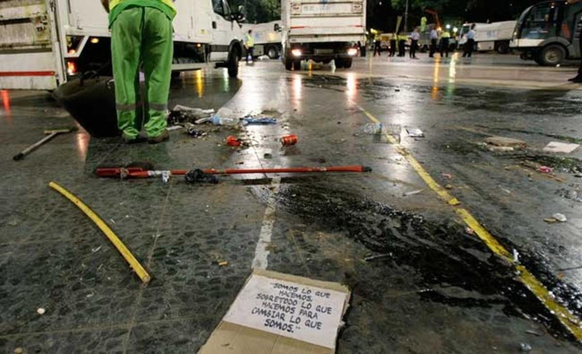 Un cartell dels indignats a terra mentre un treballador del cos de neteja de l’Ajuntament escombra la plaça.