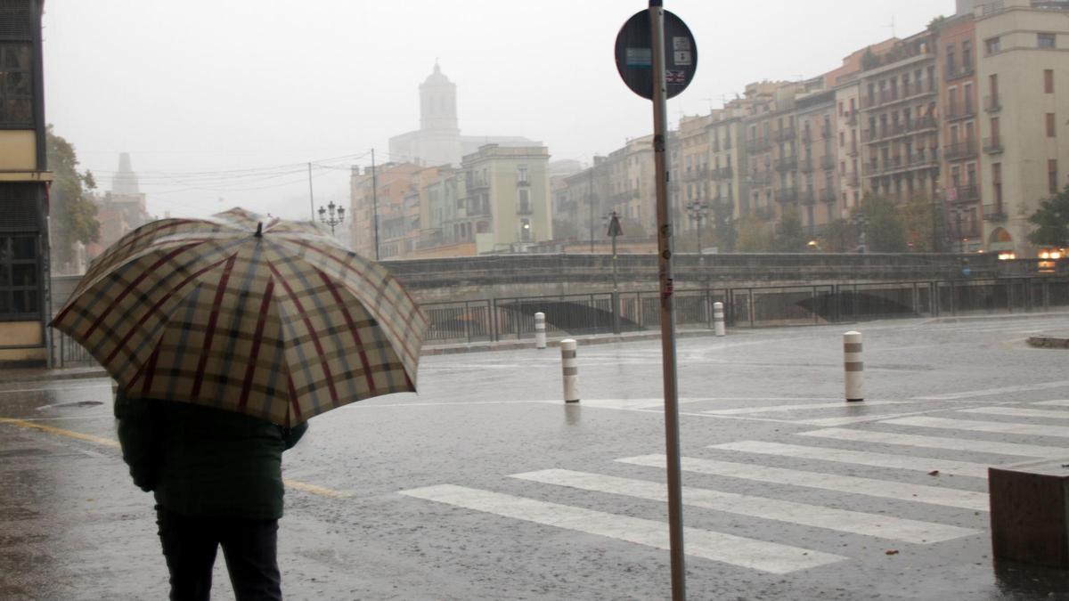 Un home amb un paraigua passeja sota la pluja, a Girona, en una imatge d'arxiu.