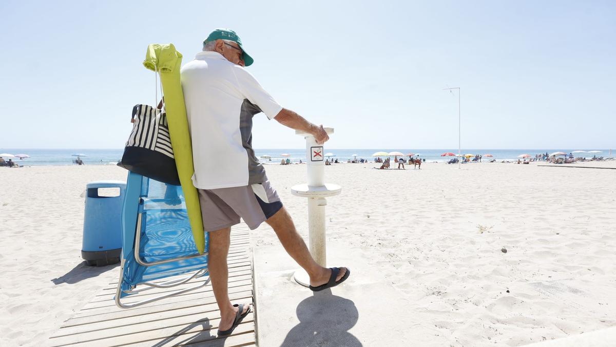 Un hombre intenta sin éxito enjuagar sus pies al salir de la playa de Muchavista