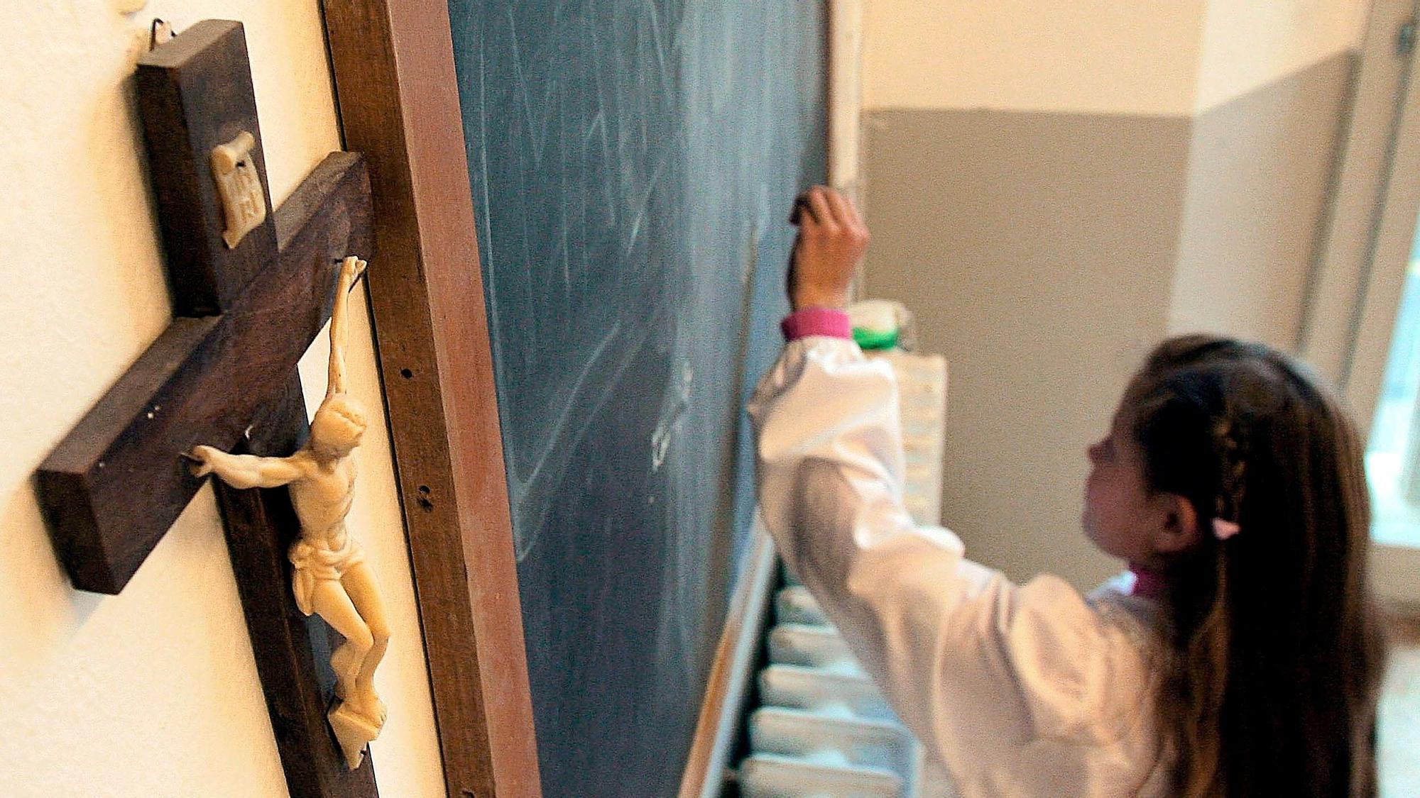 Una estudiante escribe en la pizarra de una clase que tiene un crucifijo colgado en la pared.