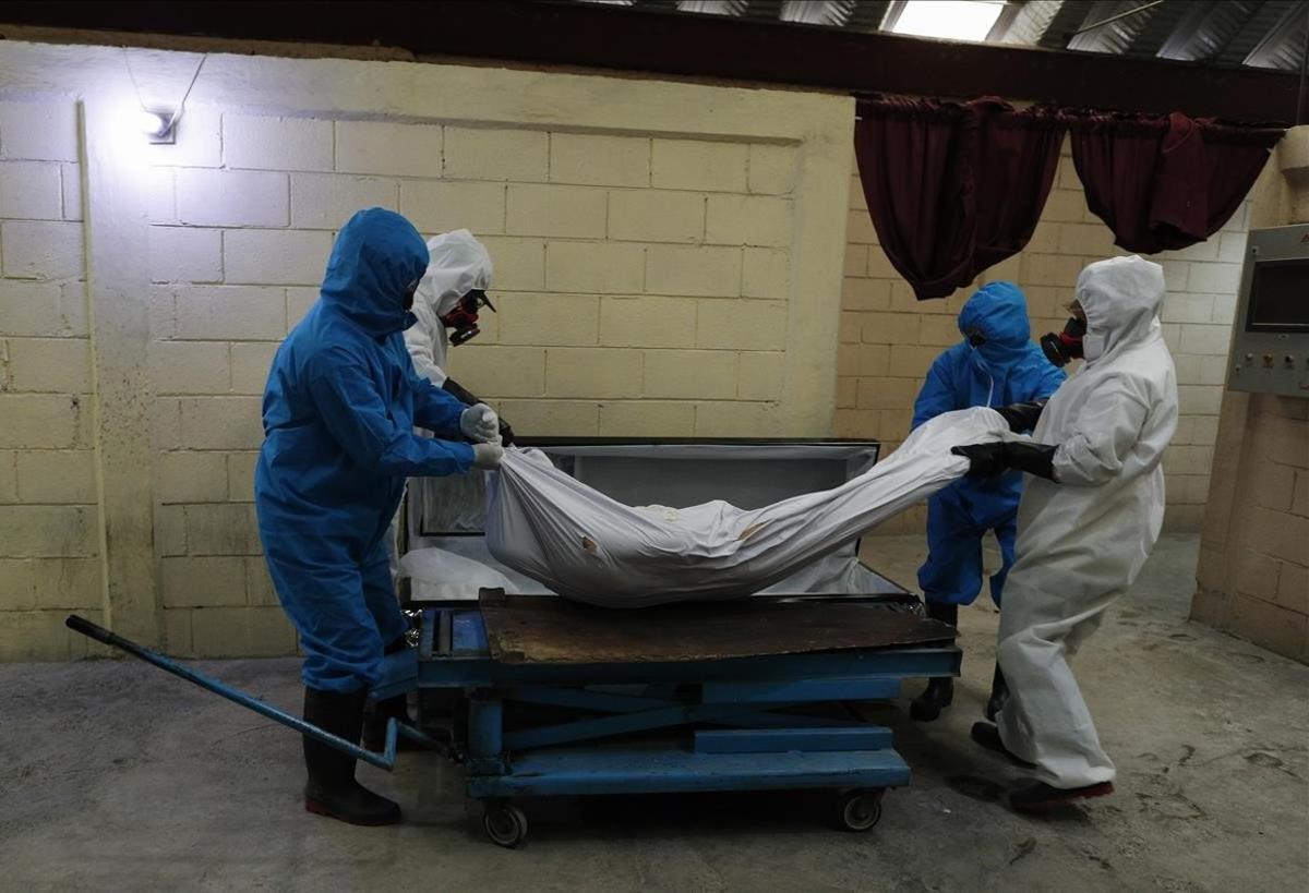 Los trabajadores de un crematorio instalan el cuerpo de una persona, en una camilla, poco antes de ser incinerada.