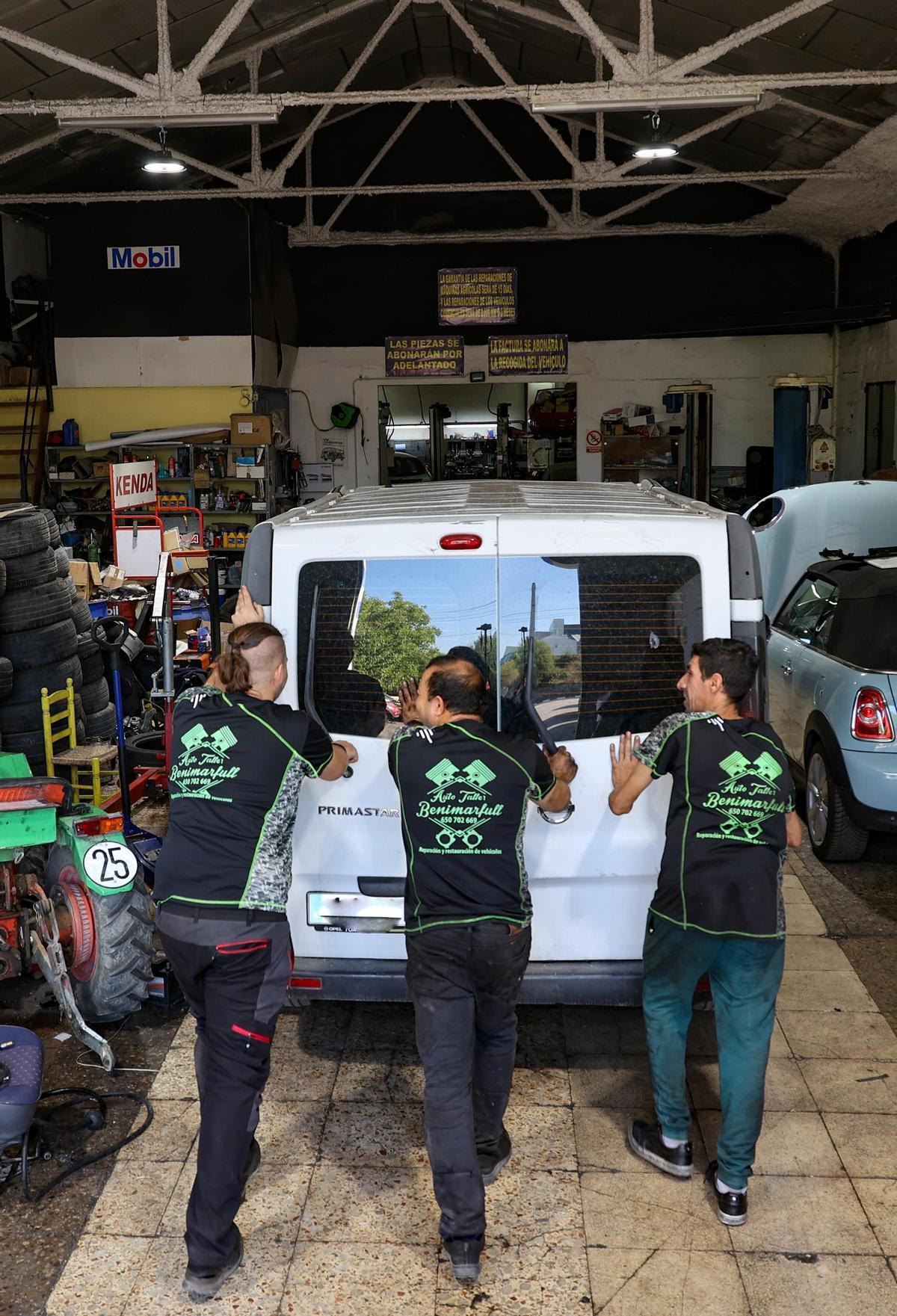 Tres mecánicos empujando una furgoneta al interior del taller para su reparación.