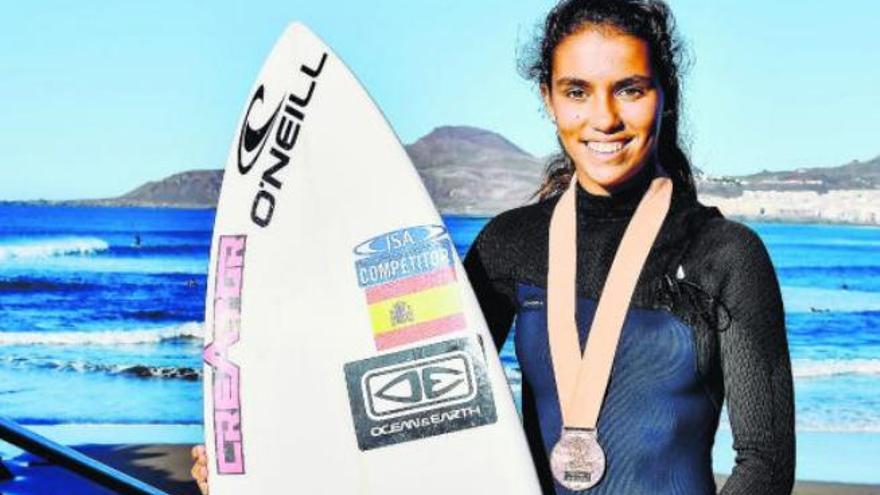 Lucía Machado posa en la Playa de La Cícer con su tabla y con la medalla conseguida en California.