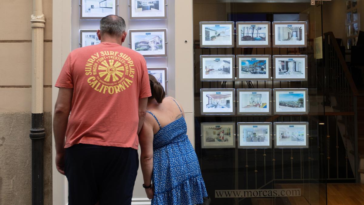 Dos personas observan los anuncios de viviendas en venta en una inmobiliaria.