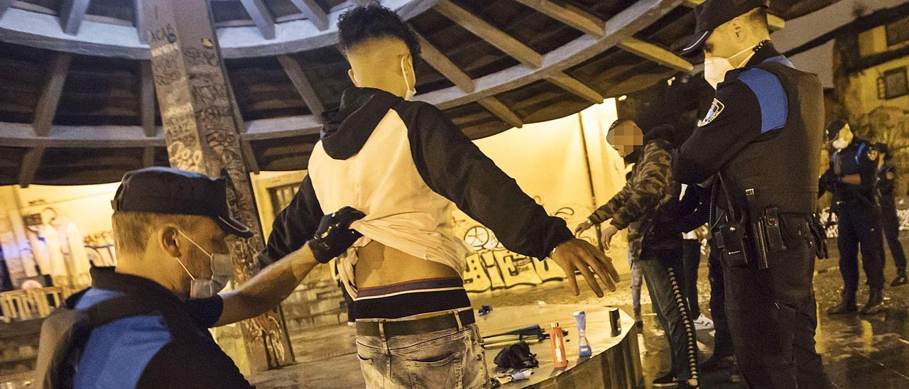 Agentes del dispositivo nocturno de la Policía Local cachean a dos individuos en la plaza del Paraguas en una intervención para evitar el botellón durante la noche del viernes. A la derecha, otro instante de la misma operación.   | MIKI LÓPEZ