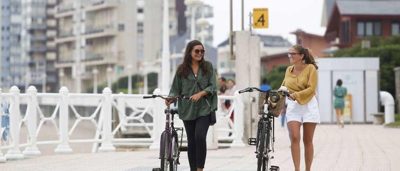 Alicia Azpiroz y Lucía Forcada llevan sus bicicletas en la mano por el paseo de la playa de Salinas Alicia Azpiroz y Lucía Forcada llevan sus bicicletas en la mano por el paseo de la playa de Salinas