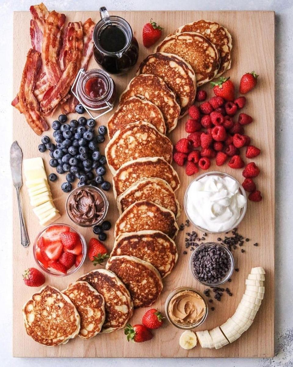 Tabla de desayuno con tortitas con mantequilla, bacon, plátano y frutos rojos