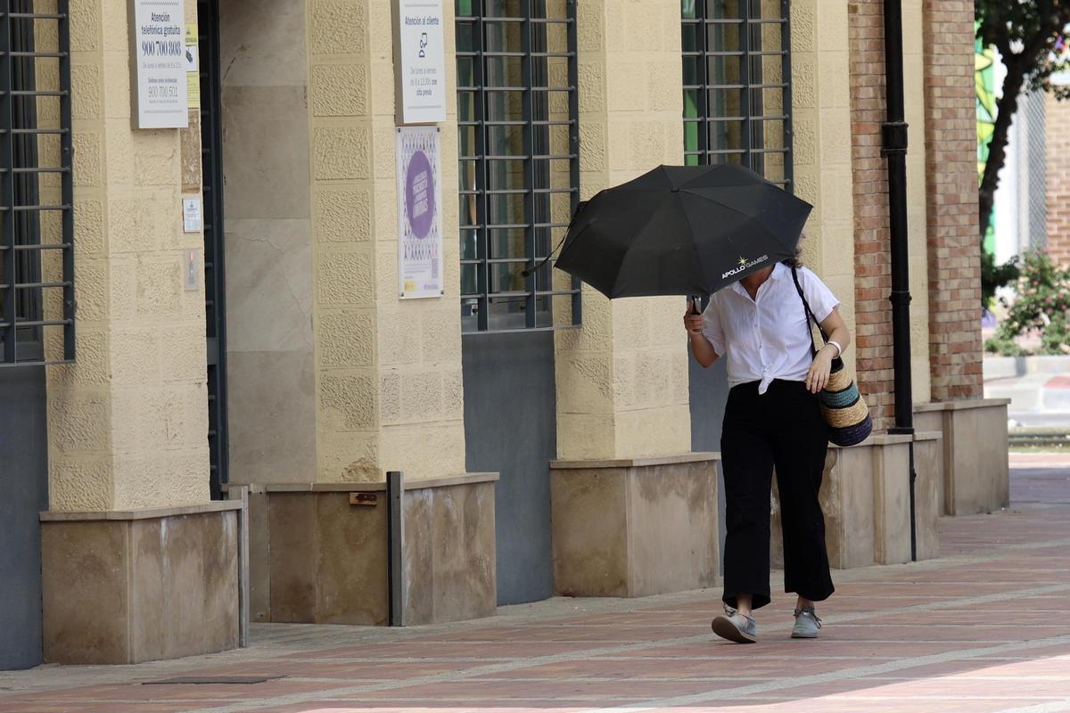 Una mujer camina junto al edificio de Aguas de Murcia bajo un sol abrasador.