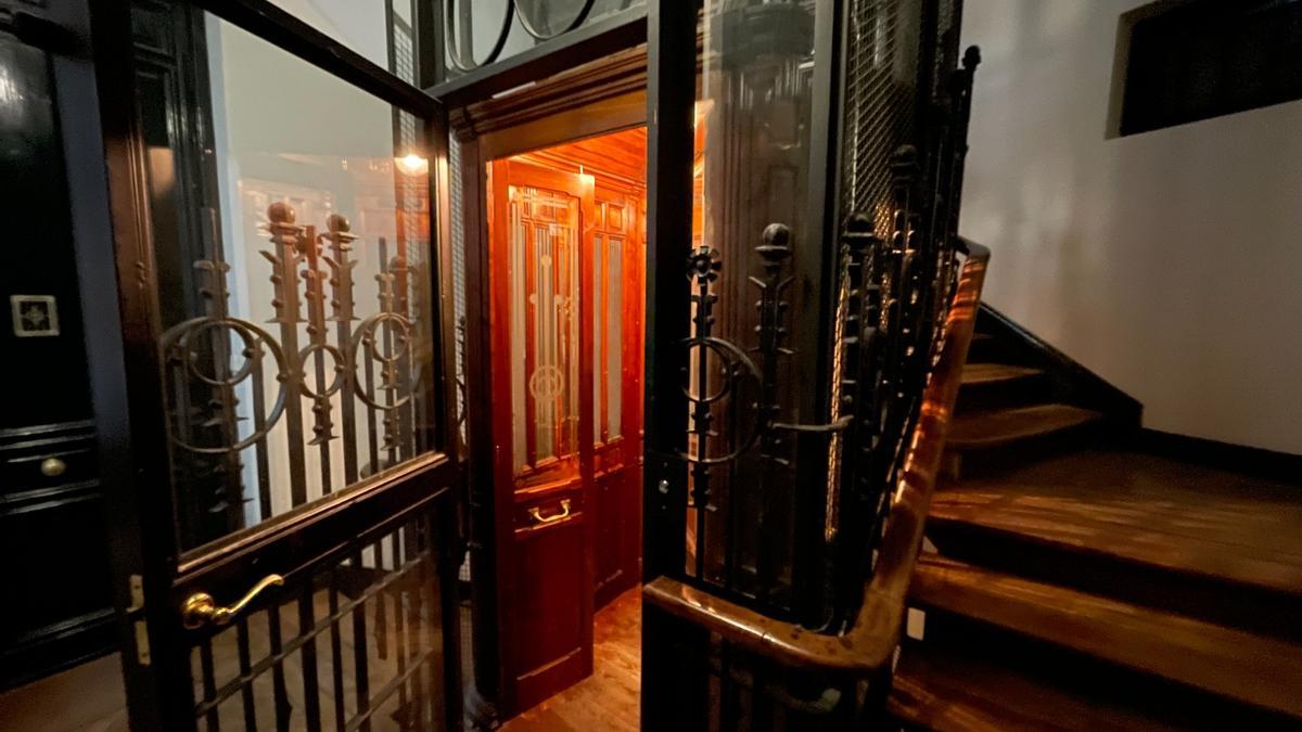Un ascensor de mediados del siglo XX, con puertas de hierro forjado que rodean una cabina de madera.