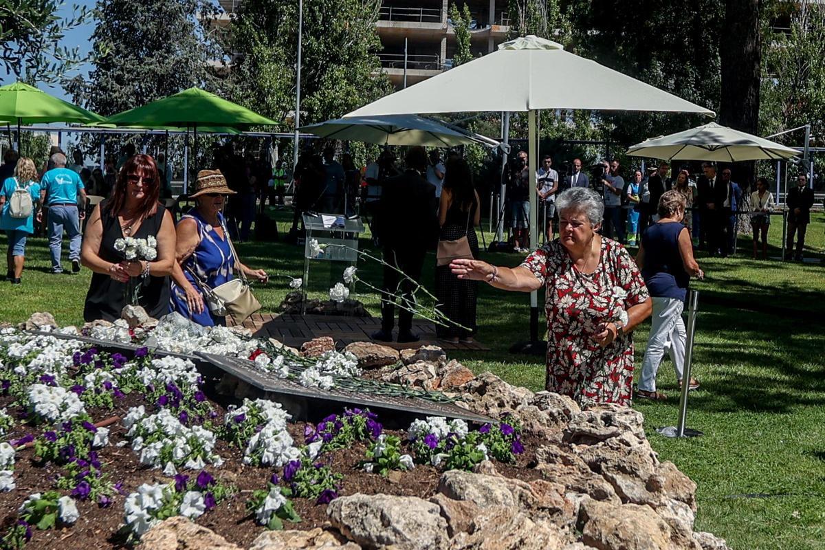 La presidenta de la Asociación de Afectados del Vuelo de Spanair JK5022, Pilar Vera, echa flores en el olivo con las placas que tienen los nombres de los fallecidos del accidente de Spanair, en la Terminal 2 del aeropuerto.