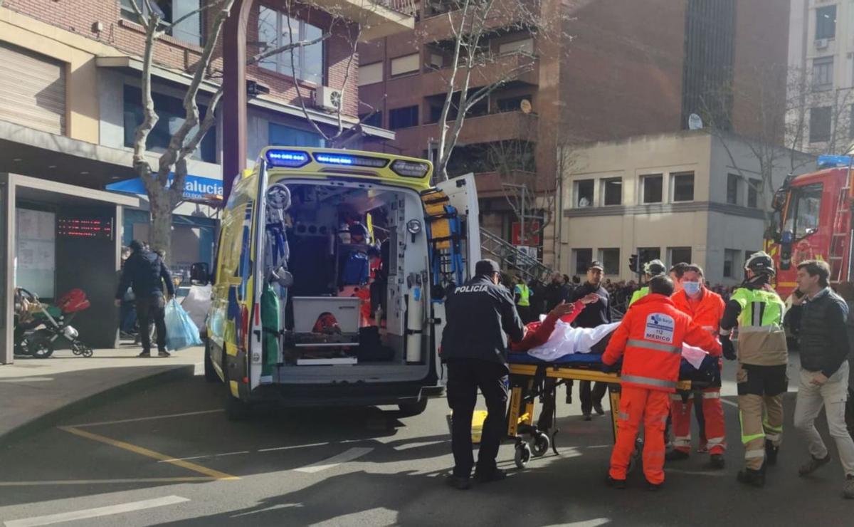 La ambulancia evacua a un lesionado y, al fondo, la mujer herida leve en la parada del autobús con su bebé. | LOZ