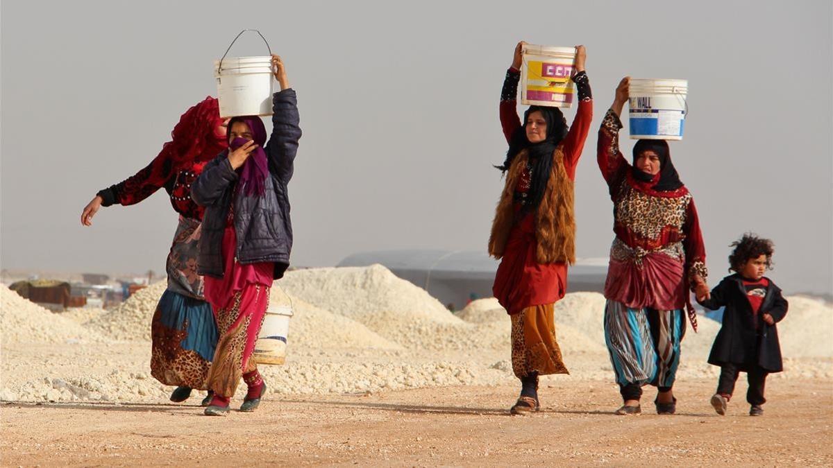 Mujeres sirias cuyas familiares han huido de los bombardeos en Idleb y la zona de Alepo cargan con cubos improvisados de agua, en un campamento de desplazados cerca de Bab al-Hawa, junto a la frontera sirioturca, el 22 de enero.