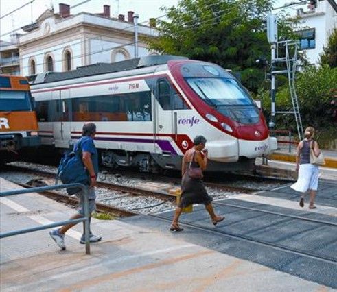 Viajeros atraviesan las vías de tren por el paso para peatones en la estación de Sant Pol.