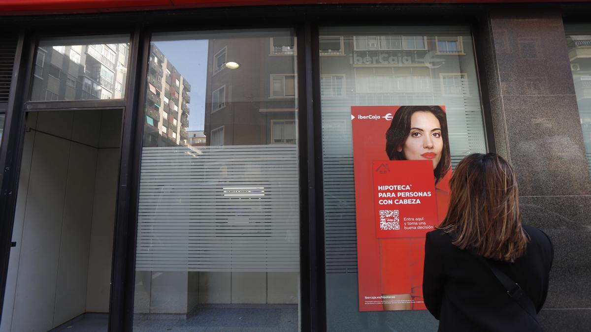 Una mujer observa una oferta de una hipoteca frente a una oficina de Ibercaja.