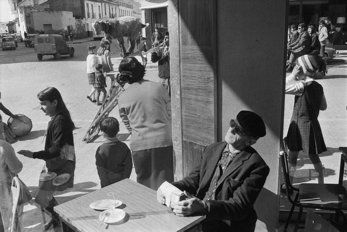 Al fondo, un trompetista gitano hace bailar a su cabra sobre una escalera, en primer plano, un hombre ciego, sentado con su radio en un bar de la Málaga de 1966.