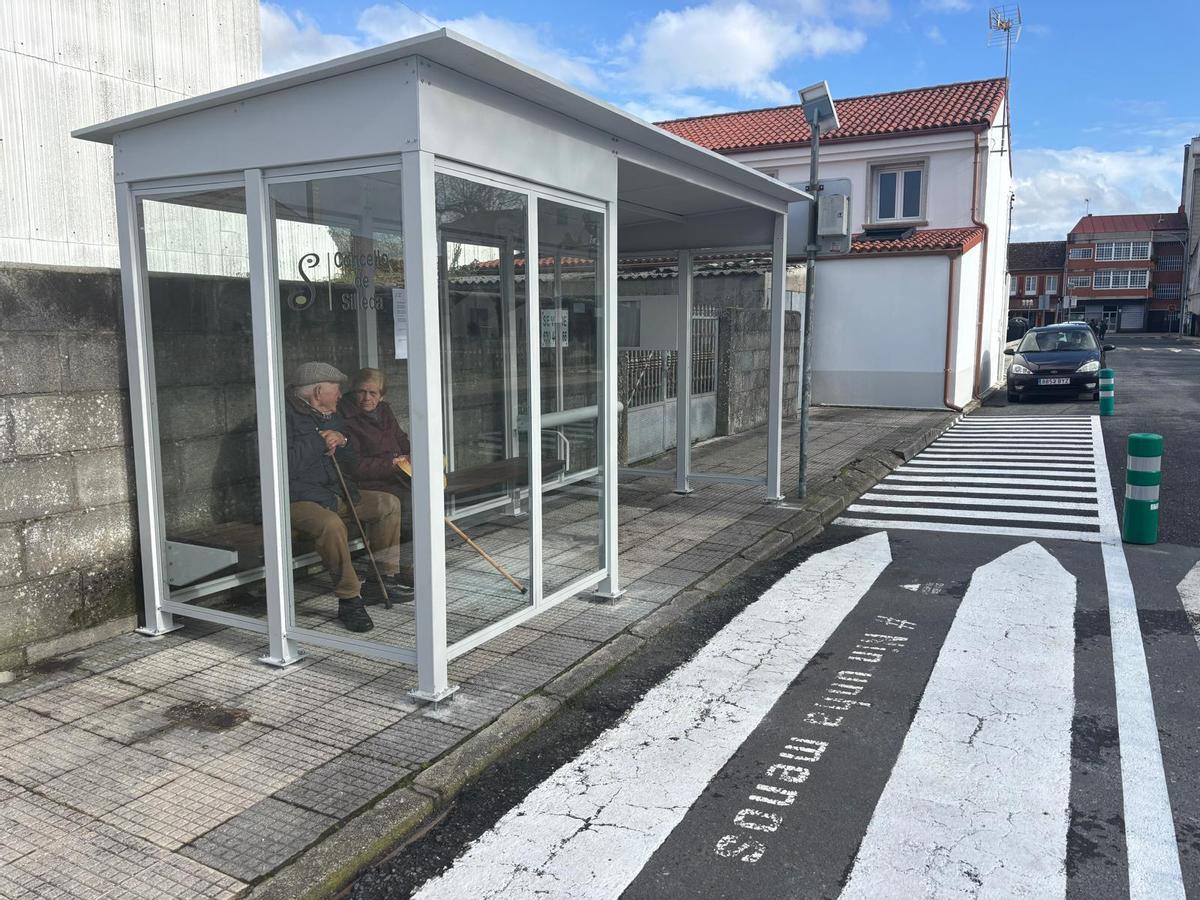 Dos personas en la nueva marquesina del transporte escolar de A Bandeira.