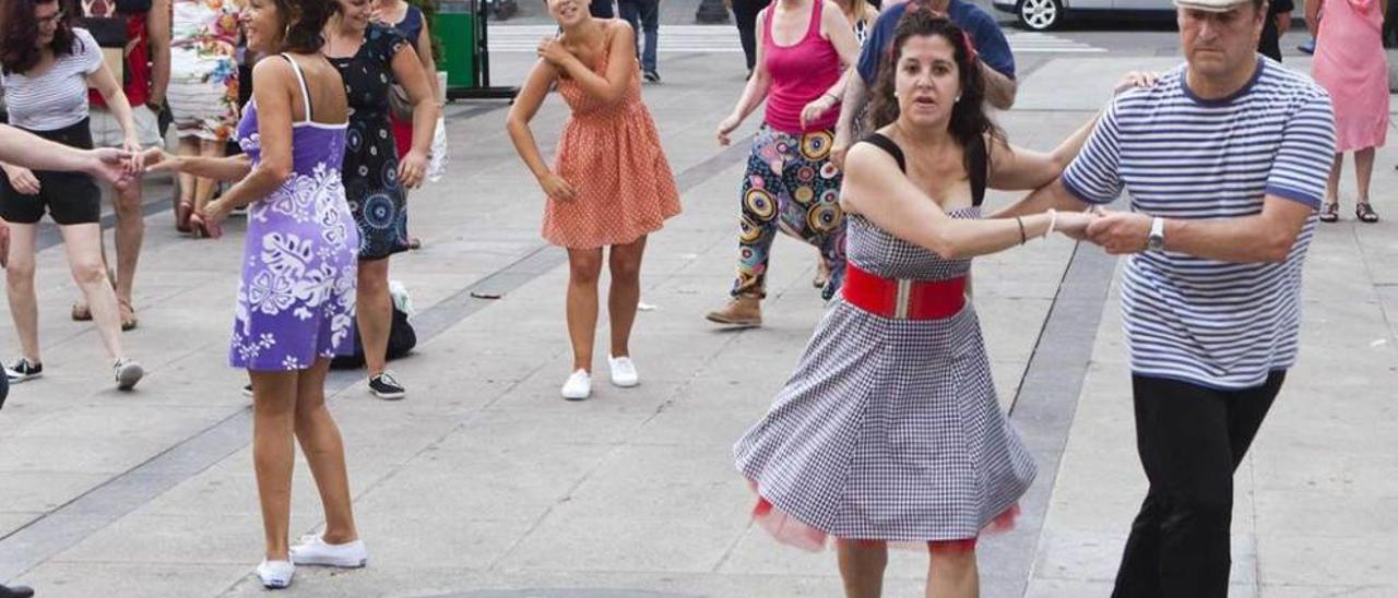 Arriba, Fini Sión y su pareja bailan en el callejón de El Natahoyo; debajo, un hombre escancia sidra mientras el resto baila.