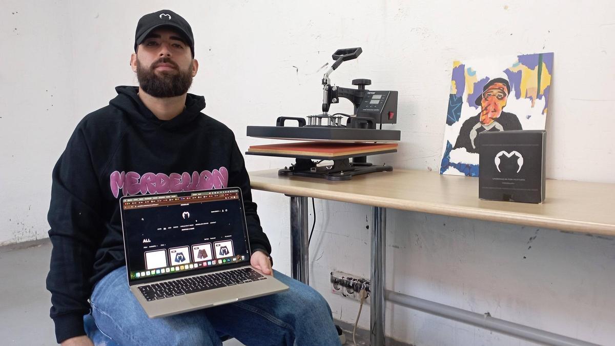 Nando Fernández, con sudadera de ‘Merdellón’ y su página web, en un rincón de su nuevo taller de La Casa Amarilla, en el Centro de Málaga.