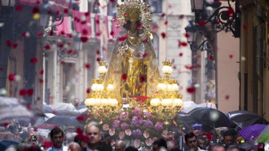 Desde un balcón lanzan petalos a la Virgen, cubierta con plástico y rodeada de público a pesar de la lluvia.