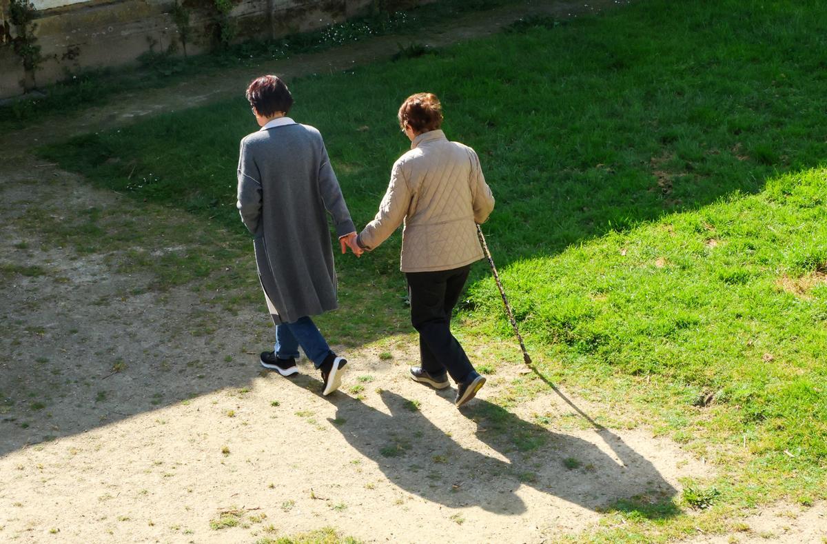 Una mujer acompaña de la mano a otra de avanzada edad.