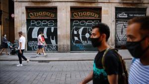 Dos hombres con mascarilla, en una calle céntrica de Barcelona con los comercios cerrados.