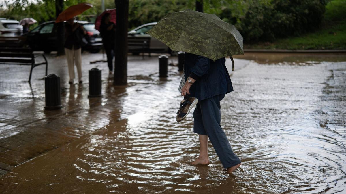 Una mujer cruza a través de la lluvia acumulada en la calle en el barrio de Canyelles-Nou Barris
