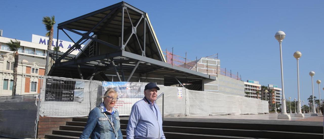 Una pareja pasa junto a la estructura de la oficina turística con el Meliá al fondo.