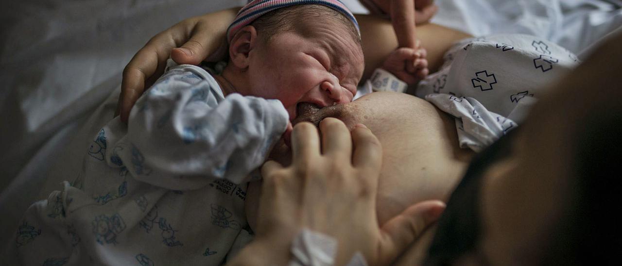 Una madre, que acaba de dar a luz en el hospital de Ourense, intentando que su bebé comience a mamar mientras el padre lo estimula. / BRAIS LORENZO