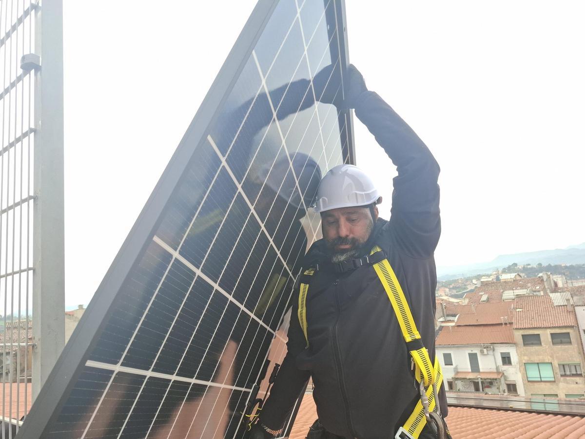 Un tècnic transporta una de les plaques fotovoltaiques de la coberta
