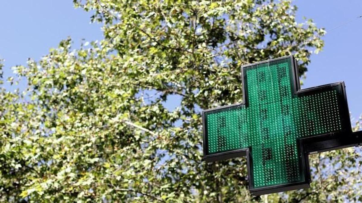Una señal luminosa de la cruz verde a la entrada de una farmacia