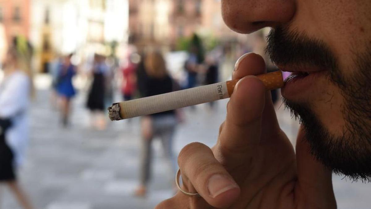 Un hombre se lleva un cigarrillo a la boca.