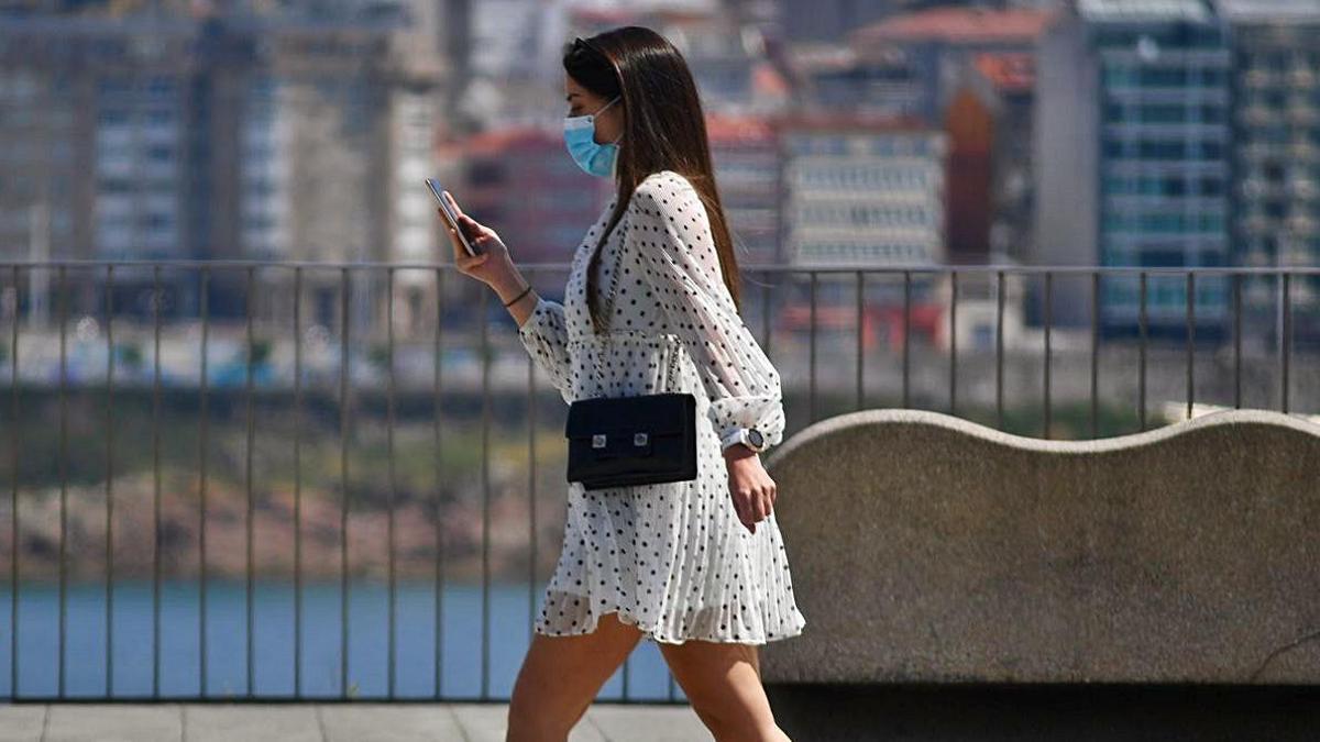 Una joven con mascarilla camina por el Paseo Marítimo de A Coruña.   | // CARLOS PARDELLAS