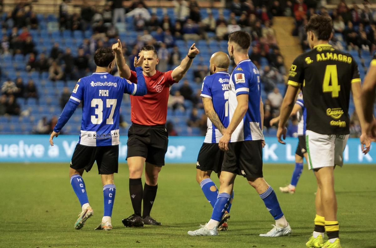El colegiado Pol Mora Arenas pide a los jugadores del Hércules que dejen de protestarle.