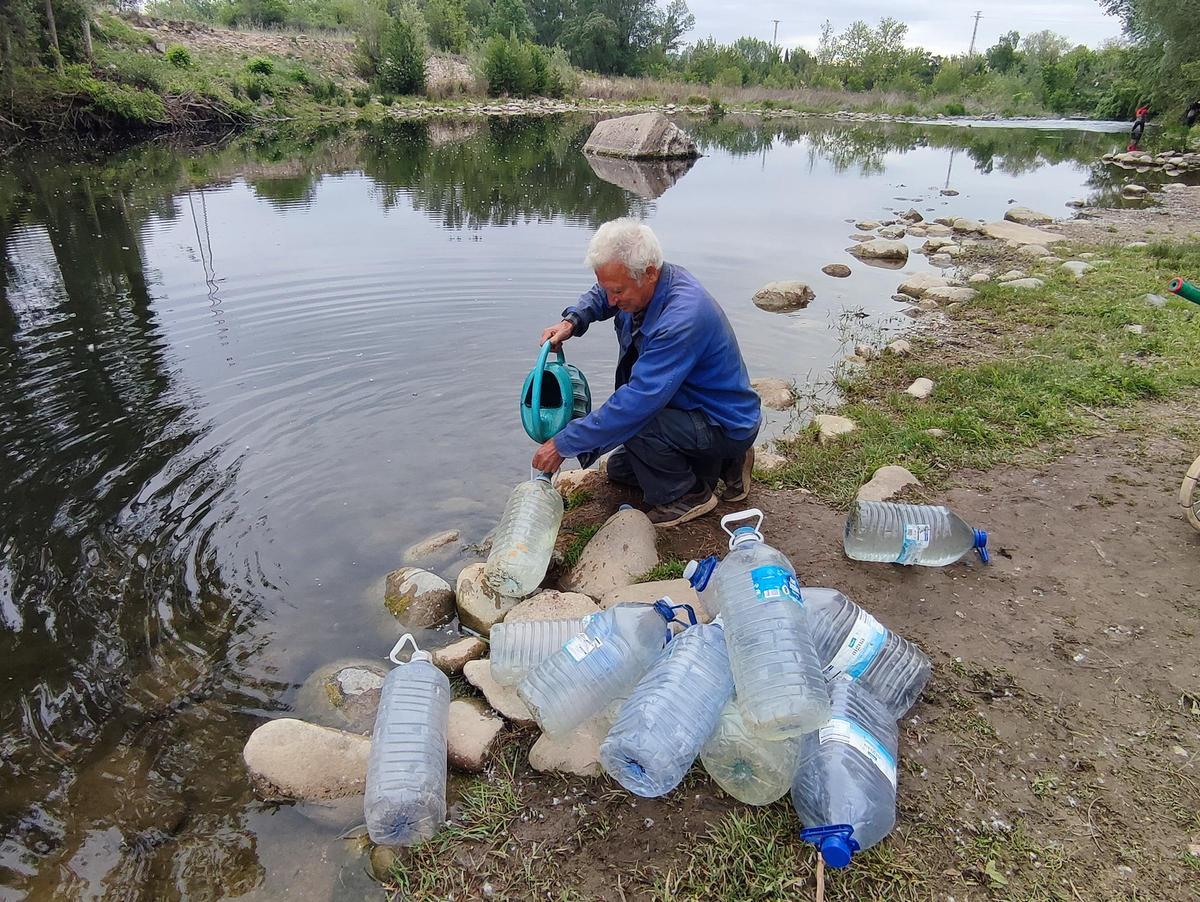 Florencio Garrido amb una regadora i onze garrafes de vuit litres, al riu Ter.