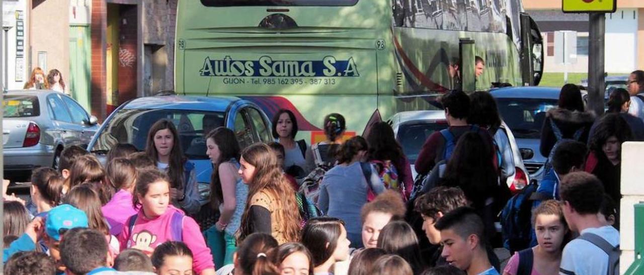 Alumnos del IES Río Nora, a la salida del centro, con un autobús escolar recogiendo usuarios al fondo.