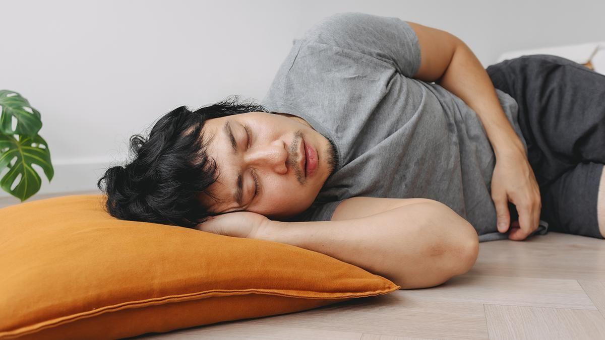 Un hombre durmiendo en el suelo con una almohada.