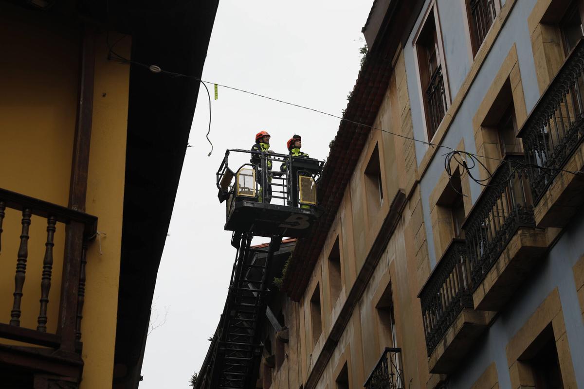 Bomberos inspeccionan un alero de la calle de La Ferrería, desde el que cayeron varios cascotes.
