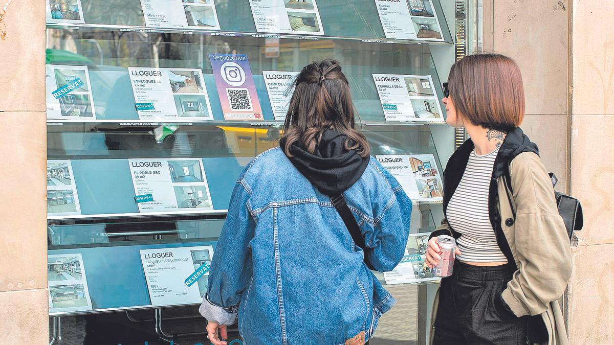 Dos jóvenes buscan ofertas de alquiler en una inmobiliaria.