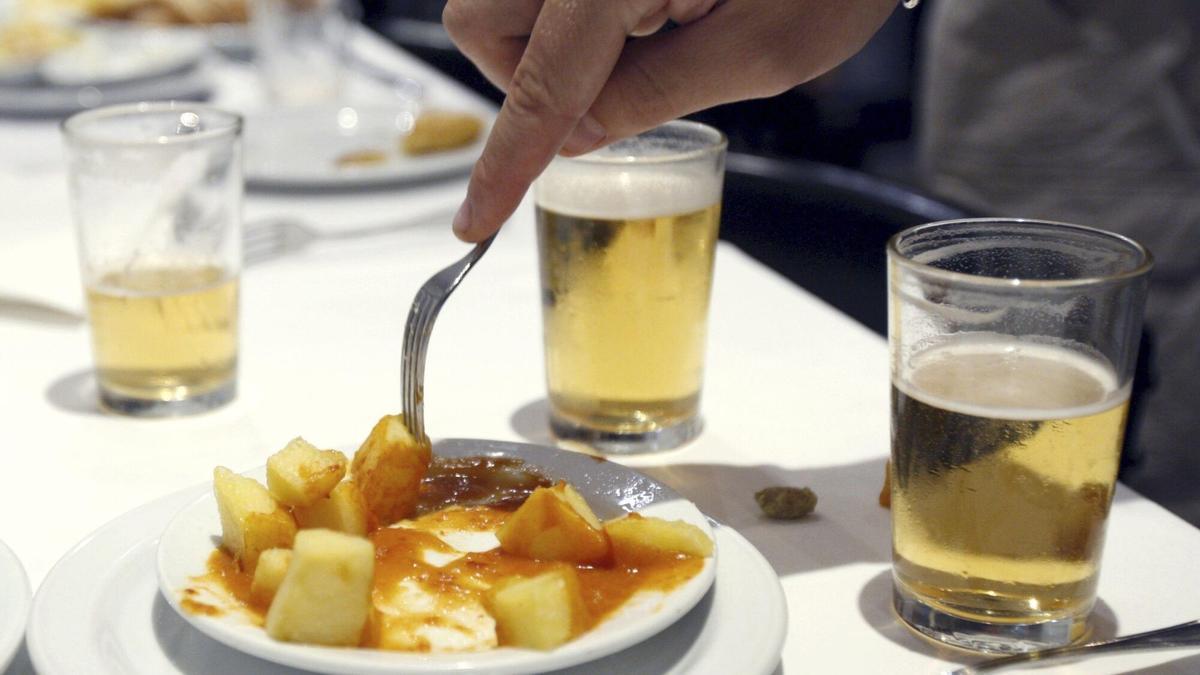 Una mesa con vasos de cerveza y unas bravas.