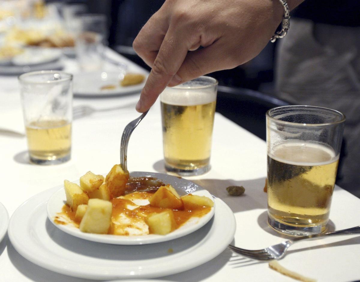 Una mesa con vasos de cerveza y unas bravas.