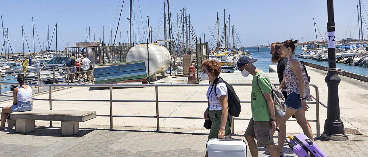 Un grupo de turistas camina junto al depósito de combustible y otros acceden a los pantalanes, en el muelle de Corralejo. |