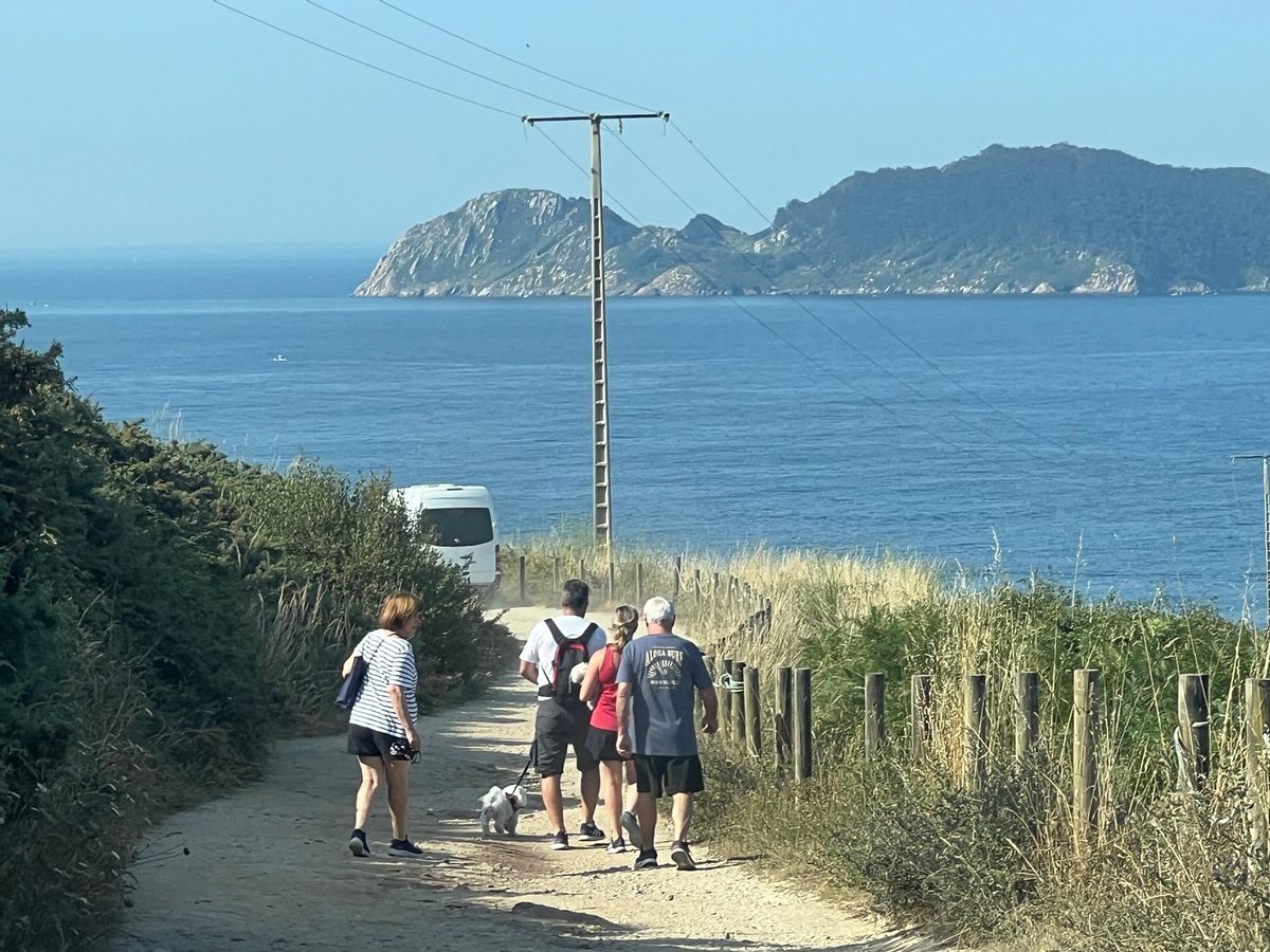 Transeúntes y vehículos, en el vial que mira a la Costa de Soavela e Illas Cíes.